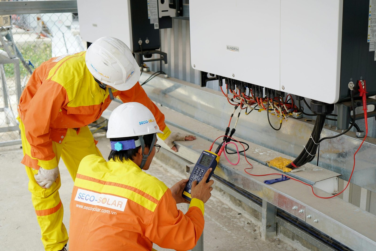 service-1 Two electrical engineers installing and testing solar power systems wearing safety gear at a construction site.
