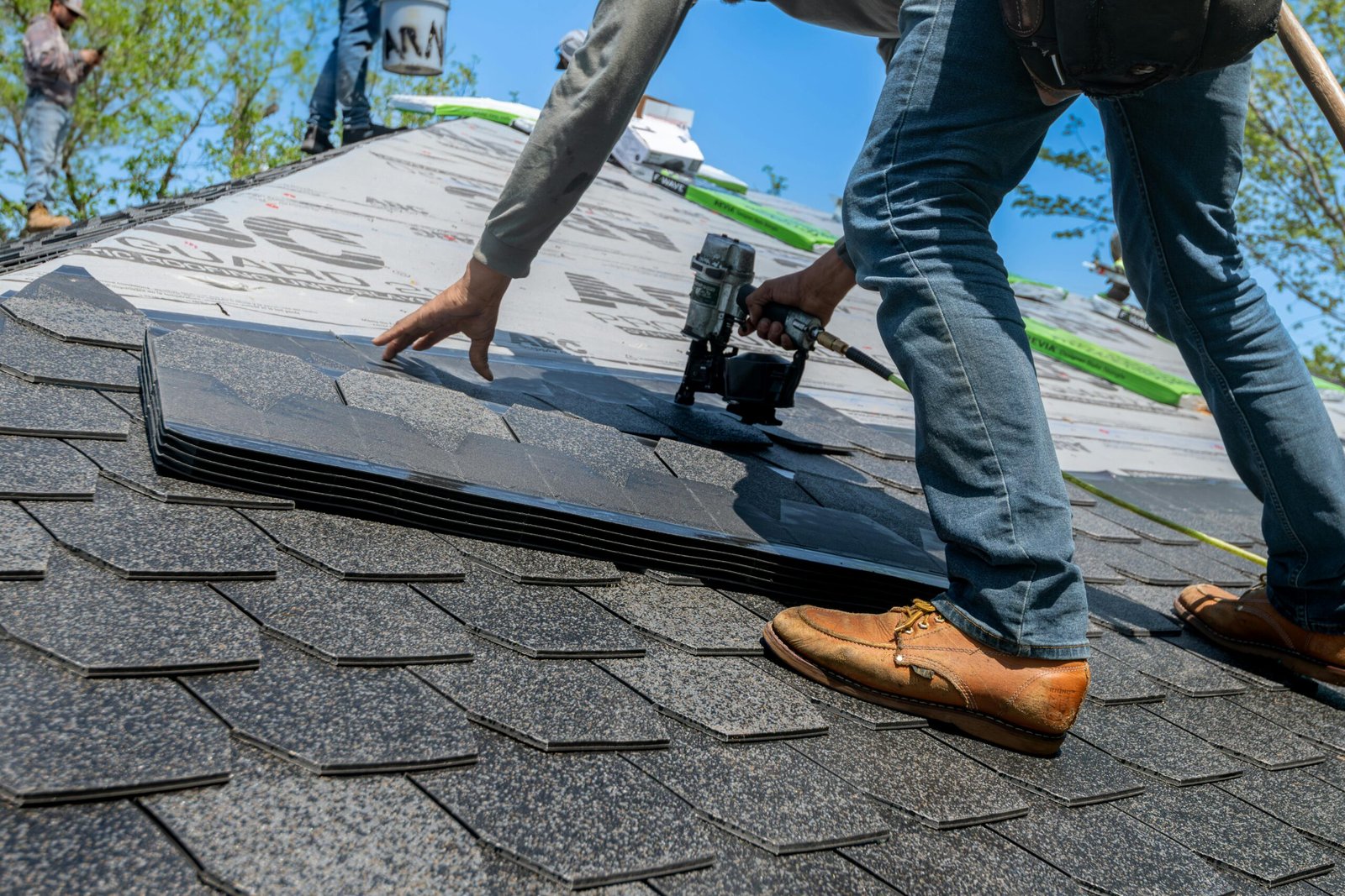 service-1 Roofer using nail gun for shingle installation on residential roof.