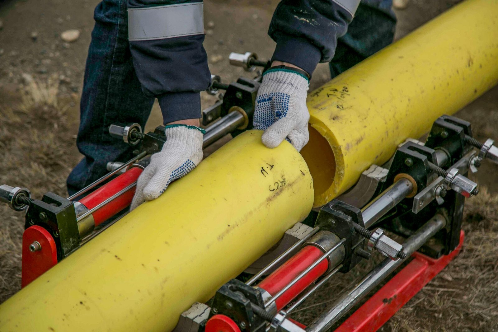 service-1 Close-up view of a worker using equipment to install yellow pipes outdoors, focusing on hands and tools.